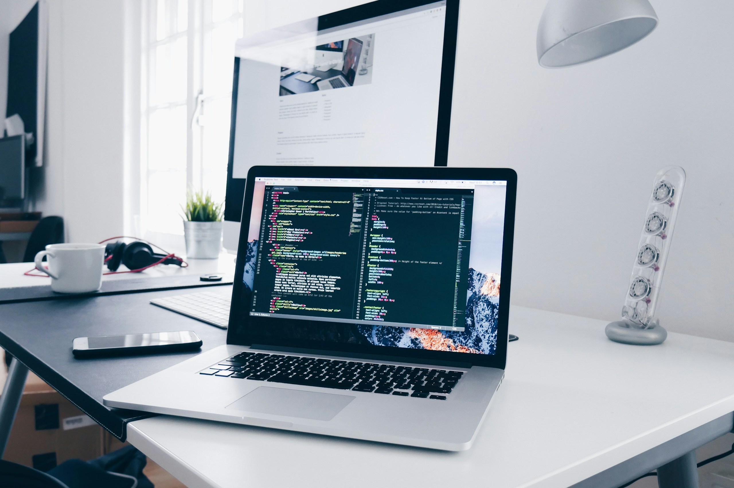 MacBook with lines of code on its screen on a busy desk