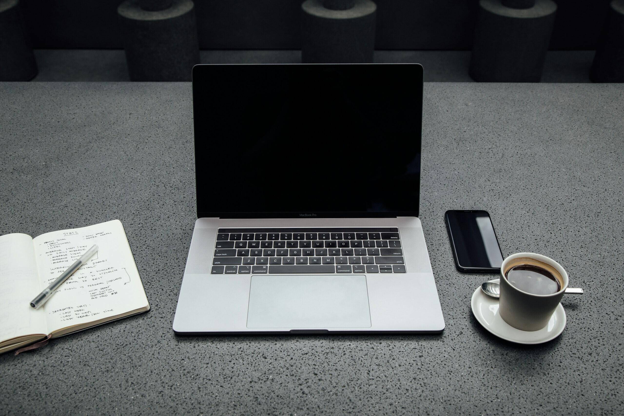 MacBook Pro beside a cup of coffee, notebook, and pen on a minimal desk